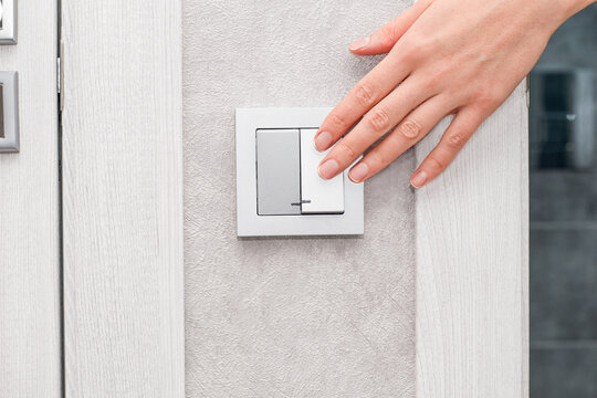 a woman's hand turns on or off the light in the bathroom with a switch on a gray wall