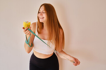 A young woman holds a measuring tape and a sweet cake in her hands. Fitness instructor. The concept...