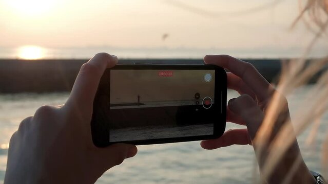 Slow motion close up of woman shooting lighhouse on smartphone at sunset