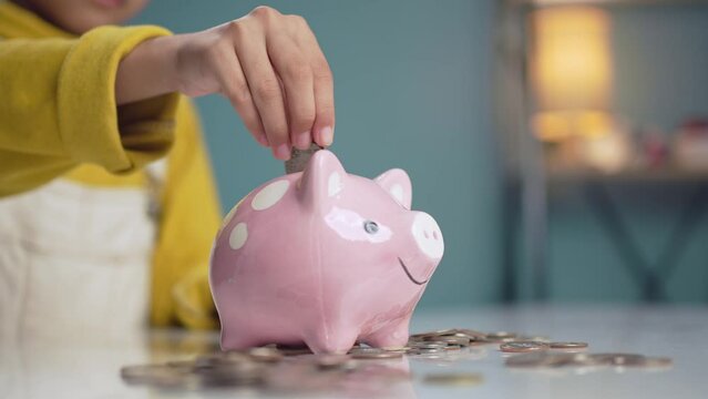 A little girl saving money by dropping a piggy bank