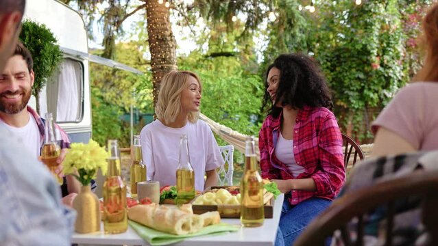 Out of town picnic, best friends hugging party celebration happy young woman enjoying friendly hugs at meeting, sitting at table, having fun spending weekend together, relaxing. Mixed racial friends.