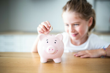 Caucasian child girl putting a coin in a pink piggy bank. Saving money for kids concept. Background with copy space.