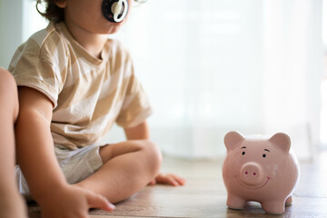Caucasian toddler with pacificator, sitting on the floor near a smiling piggy bank. Saving money...