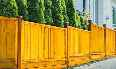 Beautiful new wooden fence around the house. Wooden fence with wooden gate with green lawn.