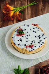 Dessert, a whole round cheesecake with blackcurrant on shortcrust pastry on a ceramic plate on a wooden background. Summer desserts, pastries with berries.