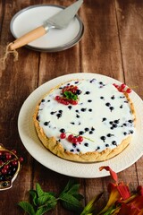 Dessert, a whole round cheesecake with blackcurrant on shortcrust pastry on a ceramic plate on a wooden background. Summer desserts, pastries with berries.