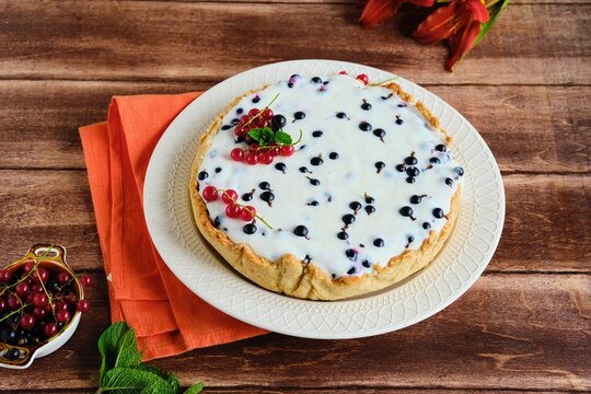 Dessert, a whole round cheesecake with blackcurrant on shortcrust pastry on a ceramic plate on a wooden background. Summer desserts, pastries with berries.