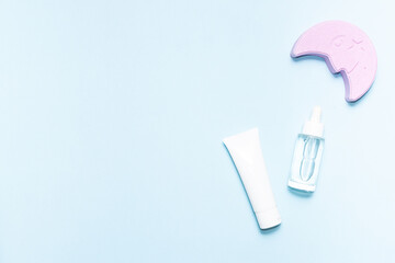 Minimalism style composition with skin care products and decorative moon on light blue background with copy space for your design. Night time cosmetic.