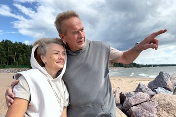 Portrait of happy elderly senior couple in love walking on a beach at summer, smile, laugh, have...