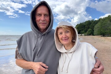 Portrait of happy elderly senior couple in love walking on a beach at summer, smile, laugh, have fun 