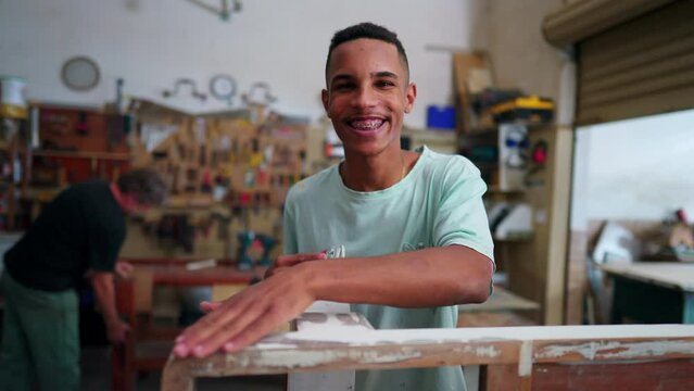 Portrait of a joyful Brazilian employee of local business smiling at camera standing inside workshop engaged with job occupation
