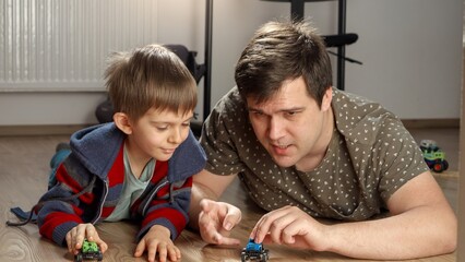 Little boy playing with his father with toy cars on floor. Children playing alone, development and education, games at home.