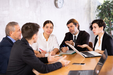 Group of confident interested business colleagues of different ages sitting at table in office, planning work in joint meeting