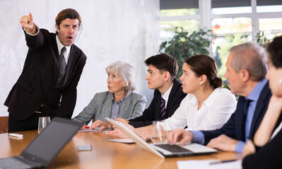 Fototapeta na wymiar Angry male boss reprehending colleagues on meeting in modern office