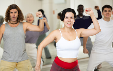 Smiling young woman rehearsing modern dance with group in dance school