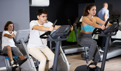Elderly man, along with other people, is engaged on an exercise bike in the gym