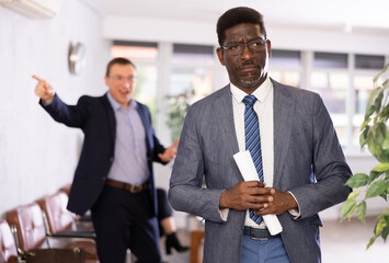 Upset adult man in business suit and glasses stands with documents in reception..