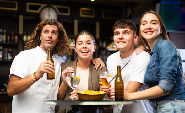Cheerful young adult friends having fun together in vintage pub, talking and drinking beer at table