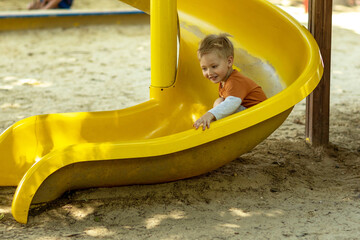 A little boy slides down a slide on a playground and laughs merrily.