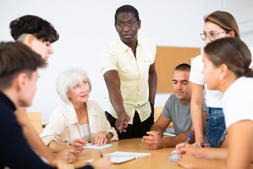 Group of interested women and men of different ages and nationalities sitting around table and communicating