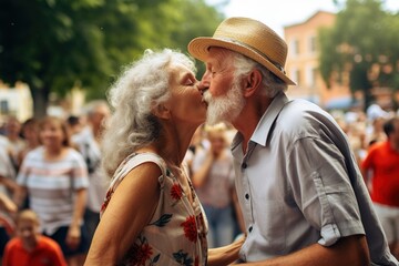 An elderly couple kissing in a crowd on the street. It is summer. The couple is wearing summer clothes.