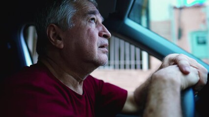 Desperate senior man gazing upwards at sky asking for God's help during hard times, sitting inside car, parked in street. Struggling older person in emotional pain