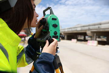 Site female  engineer operating her instrument during roadworks. Builder using total positioning station tachymeter on construction site for new road setting out