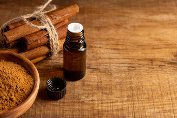 Essential cinnamon oil in a small bottle, ground cinnamon and cinnamon sticks on old wooden...