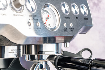 Close-up of a modern steel coffee maker with control buttons and a barometer.