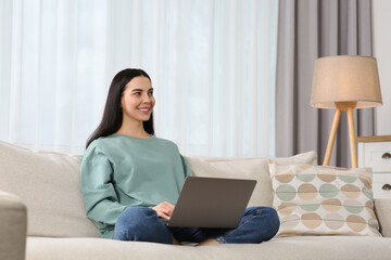 Fototapeta premium Happy woman working with laptop on sofa at home