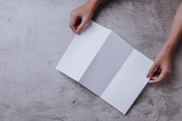 hands holding blank opened tri fold flyer brochure on gray background as template for design presentation, showcase, etc.