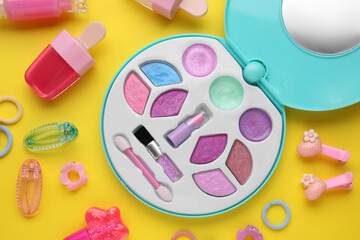 Decorative cosmetics for kids. Eye shadow palette, lipsticks and accessories on yellow background,...