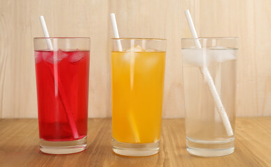 Glasses of different refreshing soda water with ice cubes and straws on wooden table