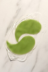 Green under eye patches with gel on white marble background, top view. Cosmetic product