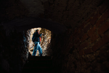 Obraz premium A tourist blogger girl in a multicolored hat and a red scarf takes photos on the ruins of an old fortress. Tourism, travel shot with copy space