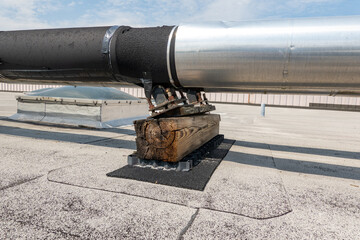 Roof mounted industrial insulated HVAC pipes on gray roof and wooden supports.	