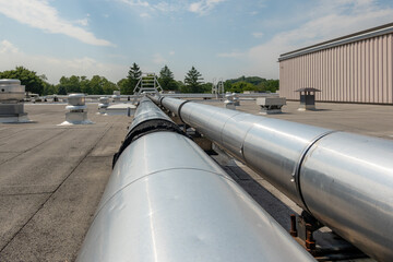 Roof mounted industrial insulated HVAC pipes on gray roof and wooden supports.	