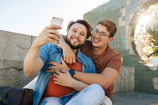 Happy caucasian gay male couple embracing and taking selfies during city walk