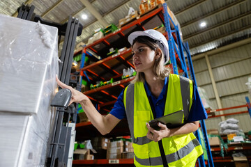Fototapeta na wymiar Female blonde hair professional worker wearing safety uniform and hard hat using digital tablet inspect goods on shelves in warehouse. women worker check stock inspecting product in factory.