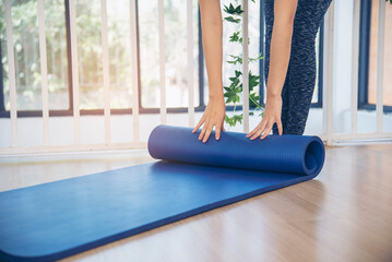 Woman hands rolled up yoga mat on gym floor in yoga fitness training room. Home workout woman close up hands rolling foam yoga gym mat. Woman barefoot home workout sportive healthy lifestyle concept