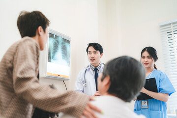A team of young Asian male doctor and female nurse in lab coat with stethoscope in conversation with patient while writing details and explaining x-ray reports in a clinic or hospital cabin