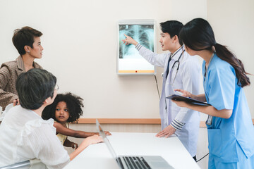 A team of young Asian male doctor and female nurse in lab coat with stethoscope in conversation with patient while writing details and explaining x-ray reports in a clinic or hospital cabin
