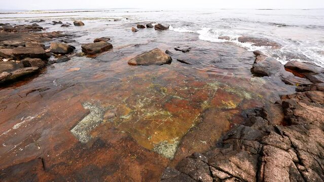 waves come ashore at a tidal pool along an Atlantic coastal shoreline with colorful rock and stone