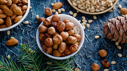 Nut assortment. Hazelnuts, almonds, pine nuts in plates stand on table with spruce branches. Top view. Background.