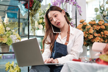 One young Asian female florist owner, working with laptop, selling floral arrange, talking on...