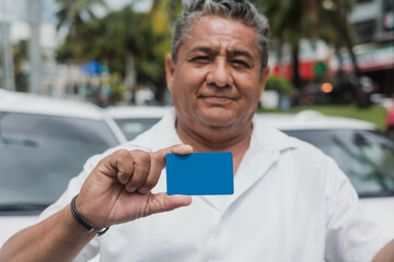 latin taxi driver man holding blank card with car on background at city street in Mexico in Latin...