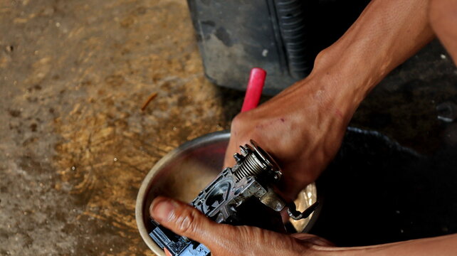 The local mechanic cleans the motorcycle carburetor with gasoline