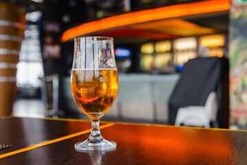 A beer in Tulip glass. Glass of light beer on wooden table in cafe or restaurant .Beautiful crystal glass with golden freshly brewed cold wheat beer stands on table cafe,restaurant terrace.