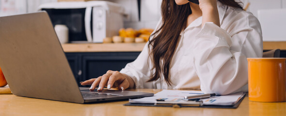 Female students note from the books at the Asian girl library sitting at sofa using laptop computer and tablet to search an online informations. in living room
