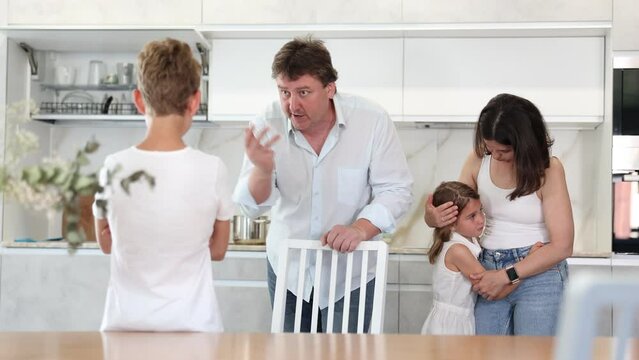 Preteen boy being scolded by angry parents in the kitchen, little sister watching him with empathy. High quality 4k footage